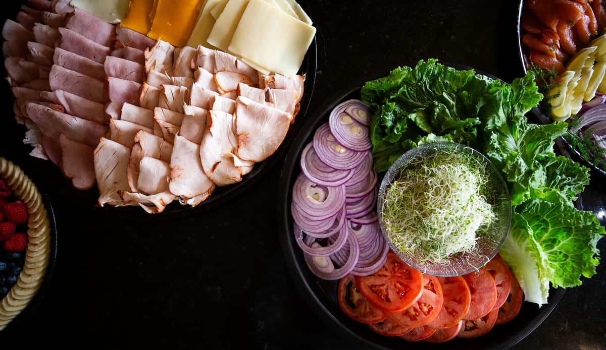 deli platter with sliced turkey, cheese, red onion, tomato, and fresh herbs arranged on a board