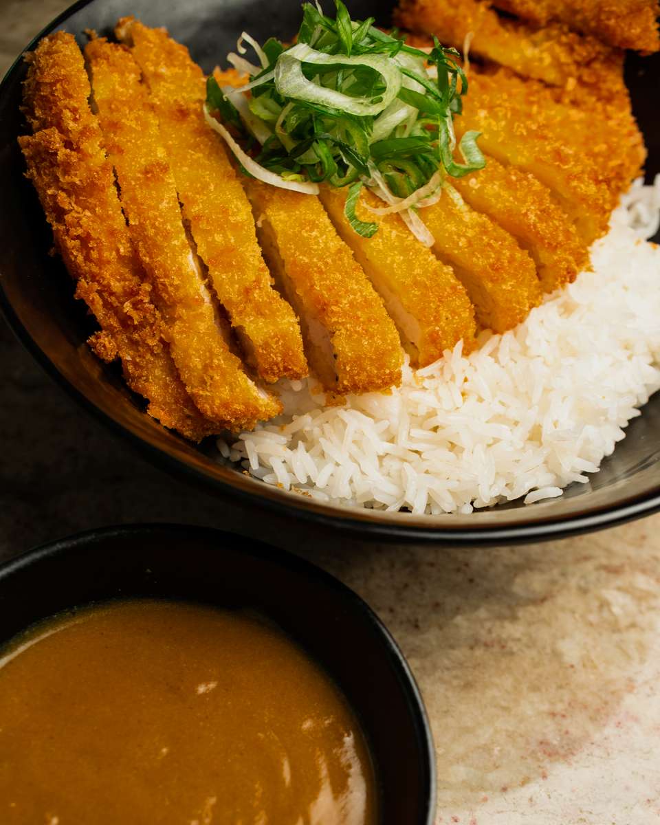 Golden crispy Japanese tonkatsu sliced over steamed white rice, topped with fresh shredded scallions and onions, served with rich curry sauce on the side in a modern restaurant setting