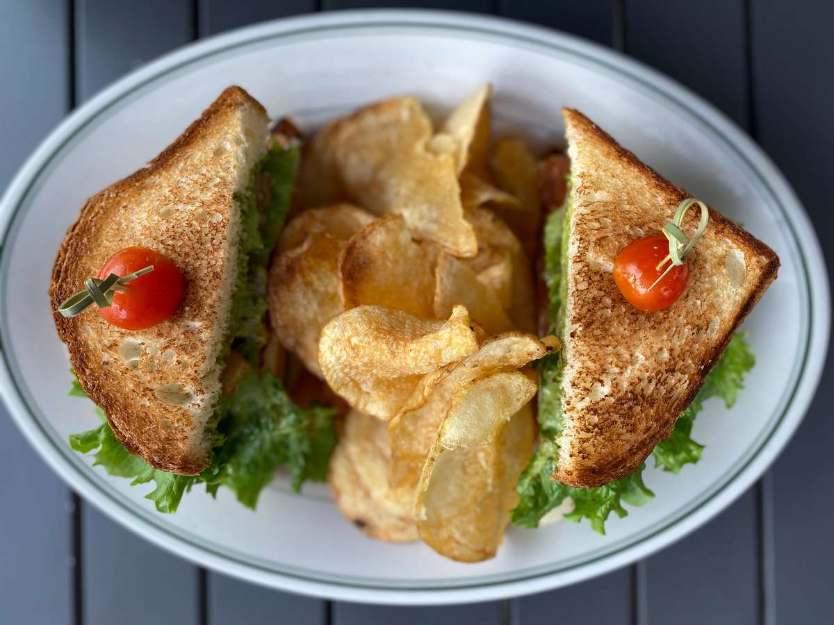 A toasted sandwich with lettuce, tomato, and crispy potato chips served on a plate from KP's Kitchen.