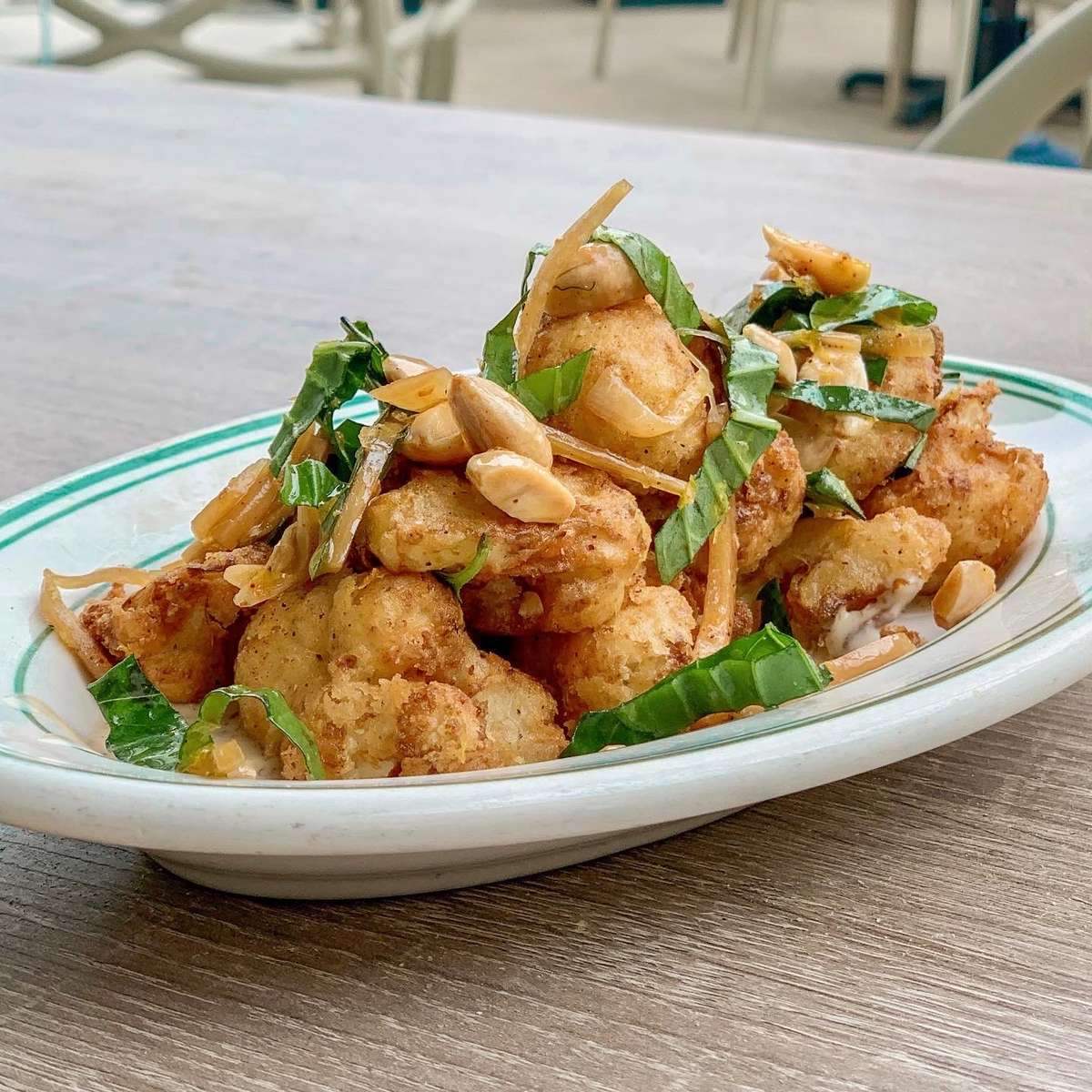 Crispy fried dish topped with peanuts and green herbs on a white plate with green rim at KP's Kitchen.