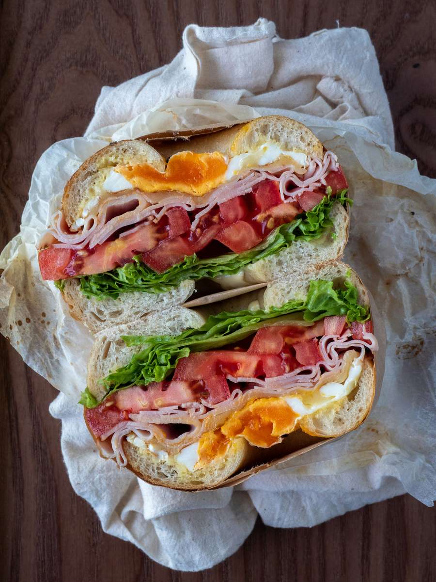 breakfast sandwich with ham, soft egg, lettuce, tomato, and melted cheese on a crusty roll
