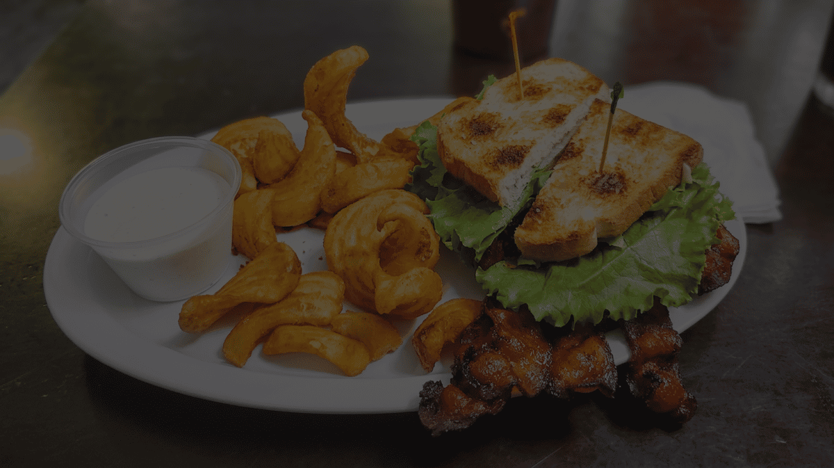 Club sandwich with ham, turkey, lettuce, tomato, and bacon, served with french fries and a pickle spear.