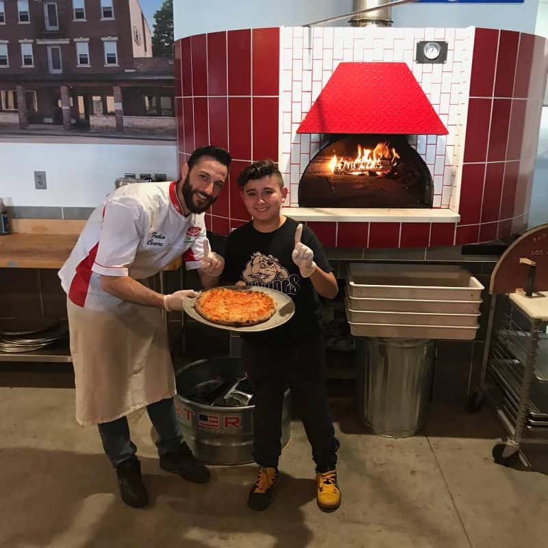 Man and child smiling infront of an oven holding a pizza