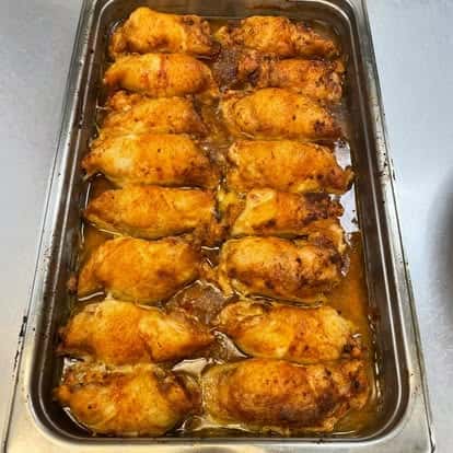 Tray of oven-baked, golden-brown chicken thighs soaking in seasoned juices, freshly prepared for serving.