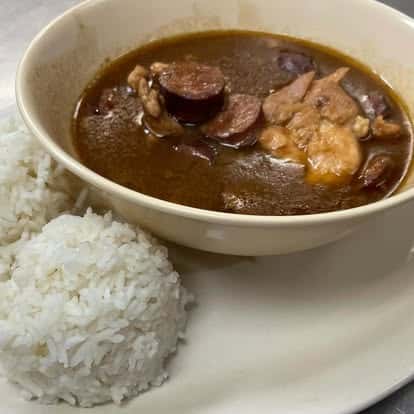 Bowl of hearty Cajun gumbo with sausage, chicken, and dark roux, served with two scoops of steamed white rice on the side.