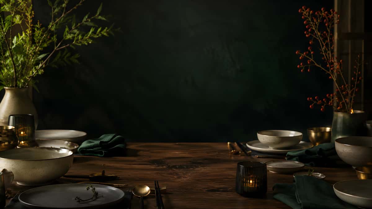 Moody restaurant dining table set with ceramic dishes, dark green linens, candlelight, and elegant botanical arrangements