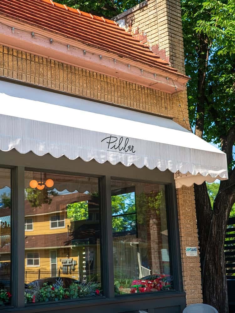 Exterior of Pillar Bistro with white scalloped awning, large front windows, and brick facade on a sunny day.