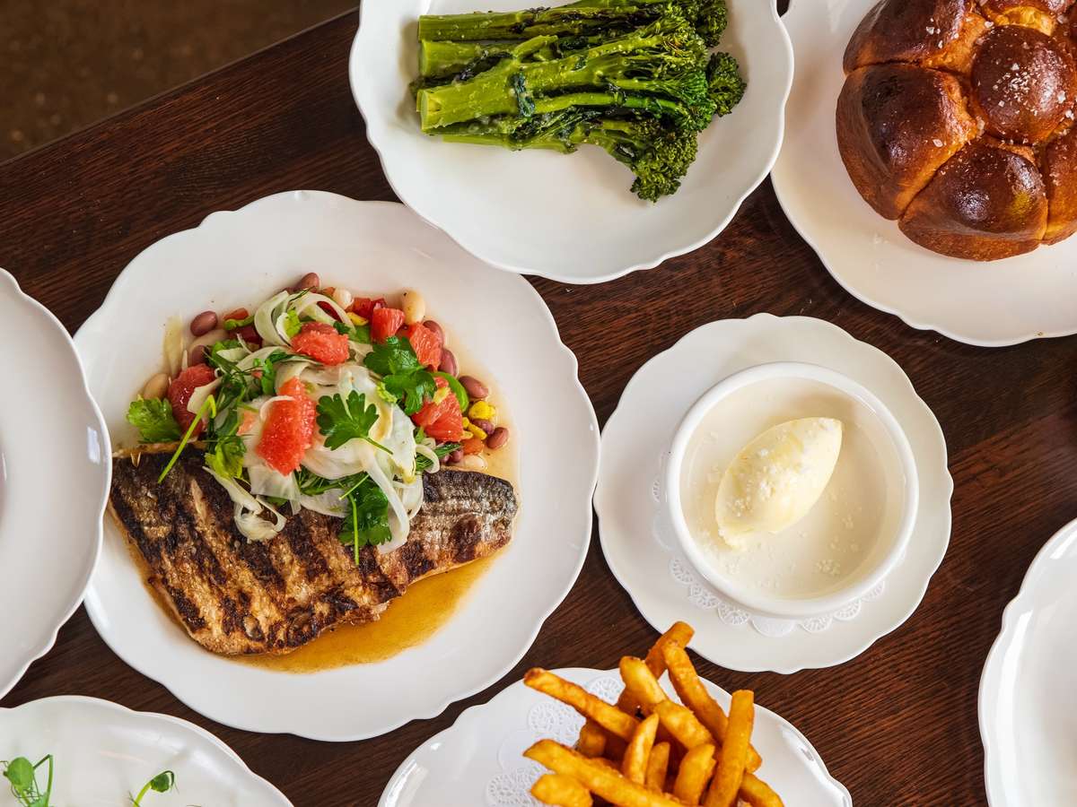 Grilled fish fillet topped with grapefruit, fennel, and beans, served alongside broccolini, brioche, fries, and a scoop of sorbet.