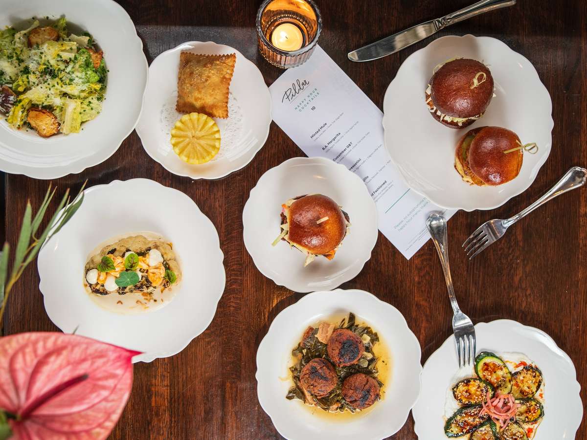 Overhead spread of small plates featuring sliders, zucchini with sesame, salad, croquettes, and a golden-fried pastry with pineapple.