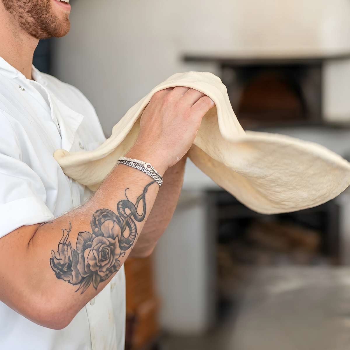 Pizza chef hand-stretching fresh dough in a restaurant kitchen near a wood-fired pizza oven