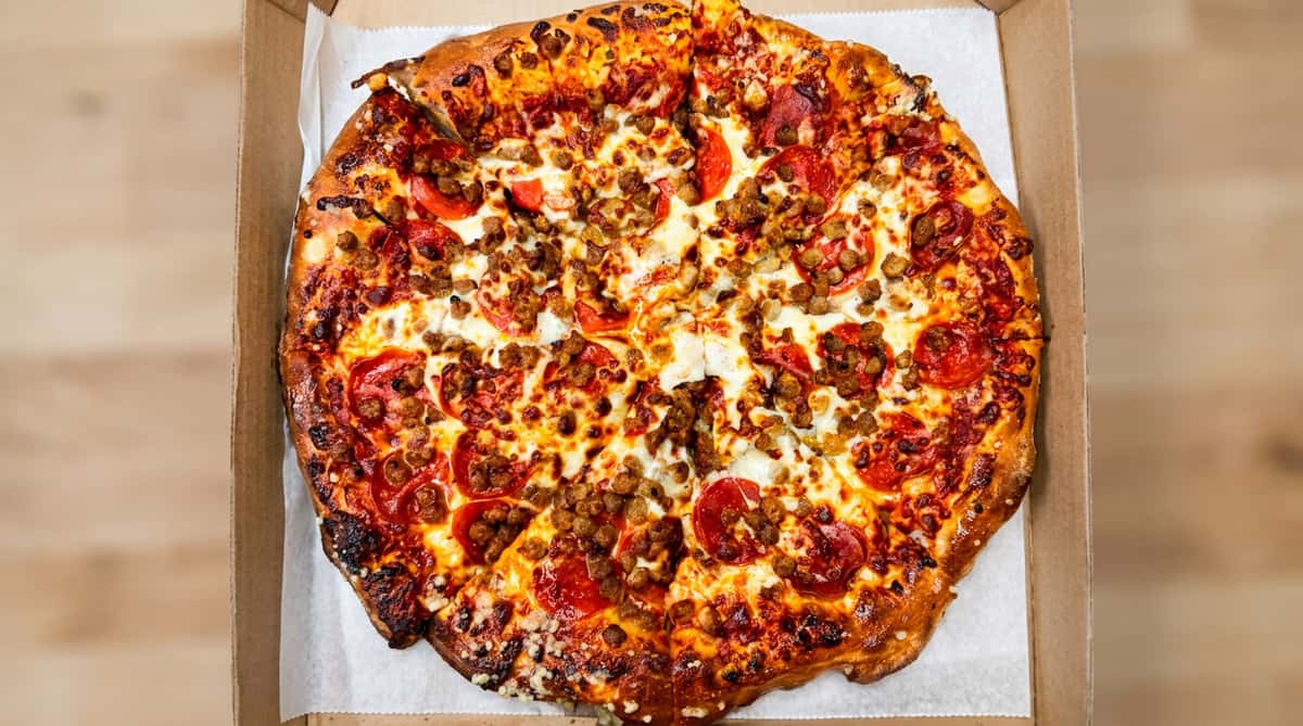Pepperoni and sausage pizza in a cardboard box, with a slice removed.