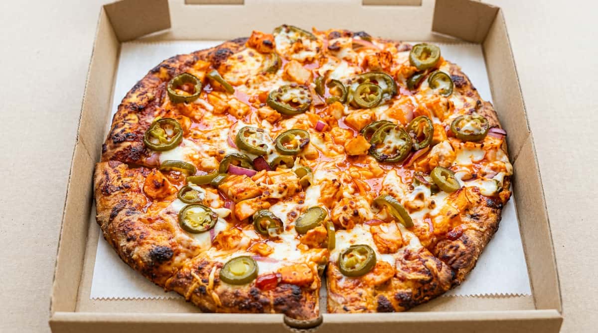 Buffalo chicken pizza with melted mozzarella, red onion, and sliced jalapeños in a pizza box.