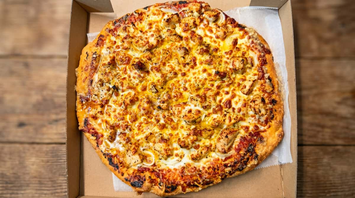 Chicken and onion pizza with melted cheese and a golden crust in a cardboard box.