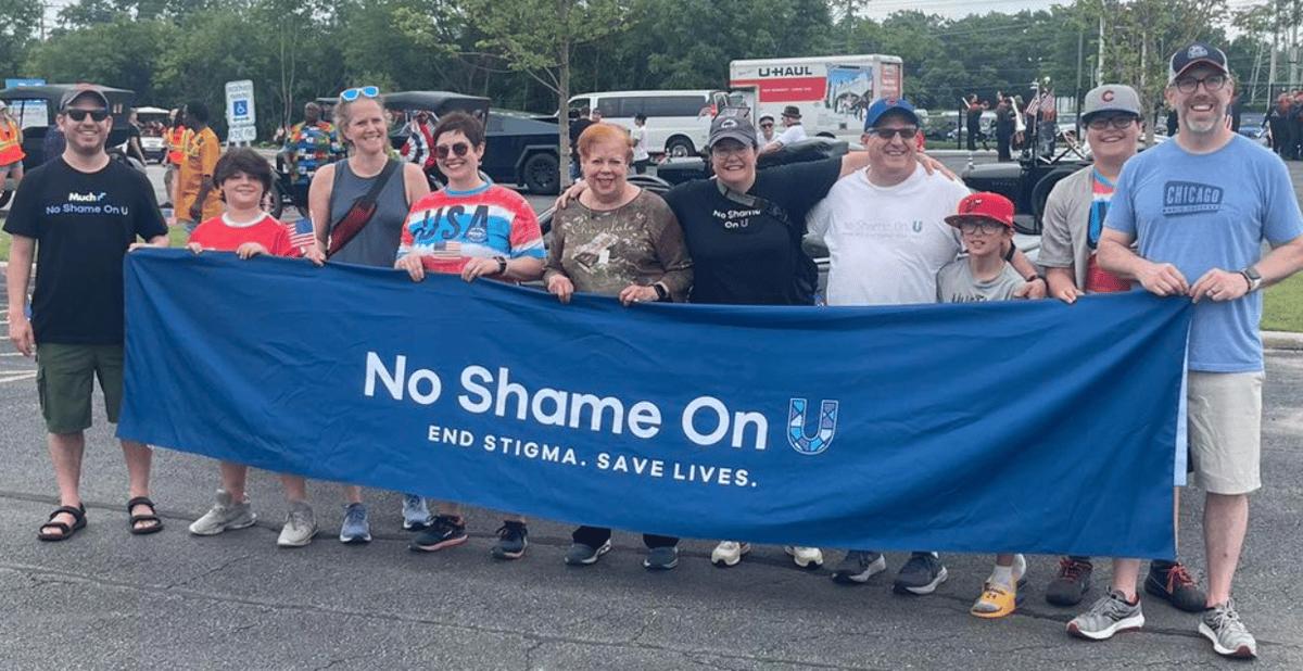group holding a navy blue banner with the No Shame on U logo