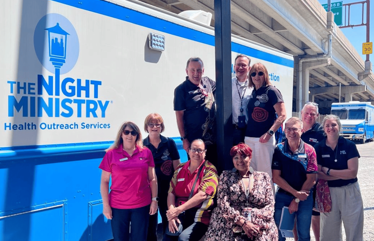 a group of people standing in front of a blue bus with the The Night Ministry Logo
