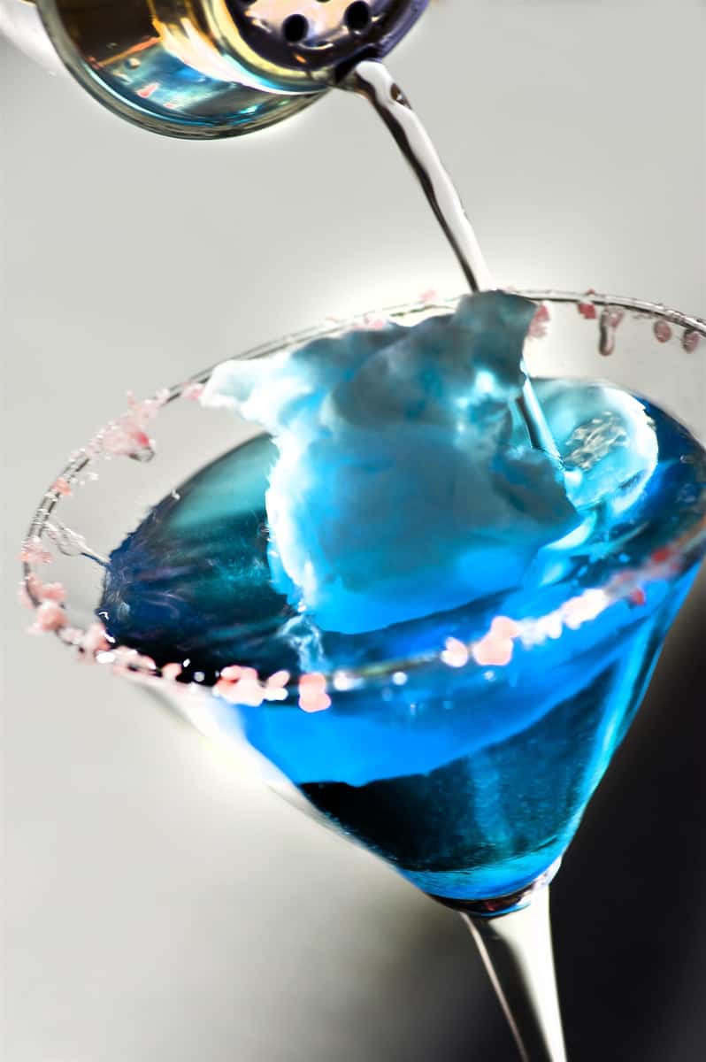 blue cocktail being poured into a glass with candy on the rim