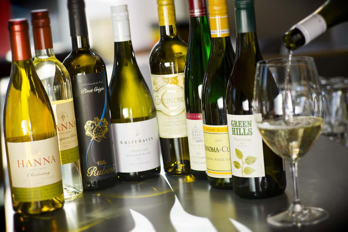 various bottles of white wine with one glass being poured