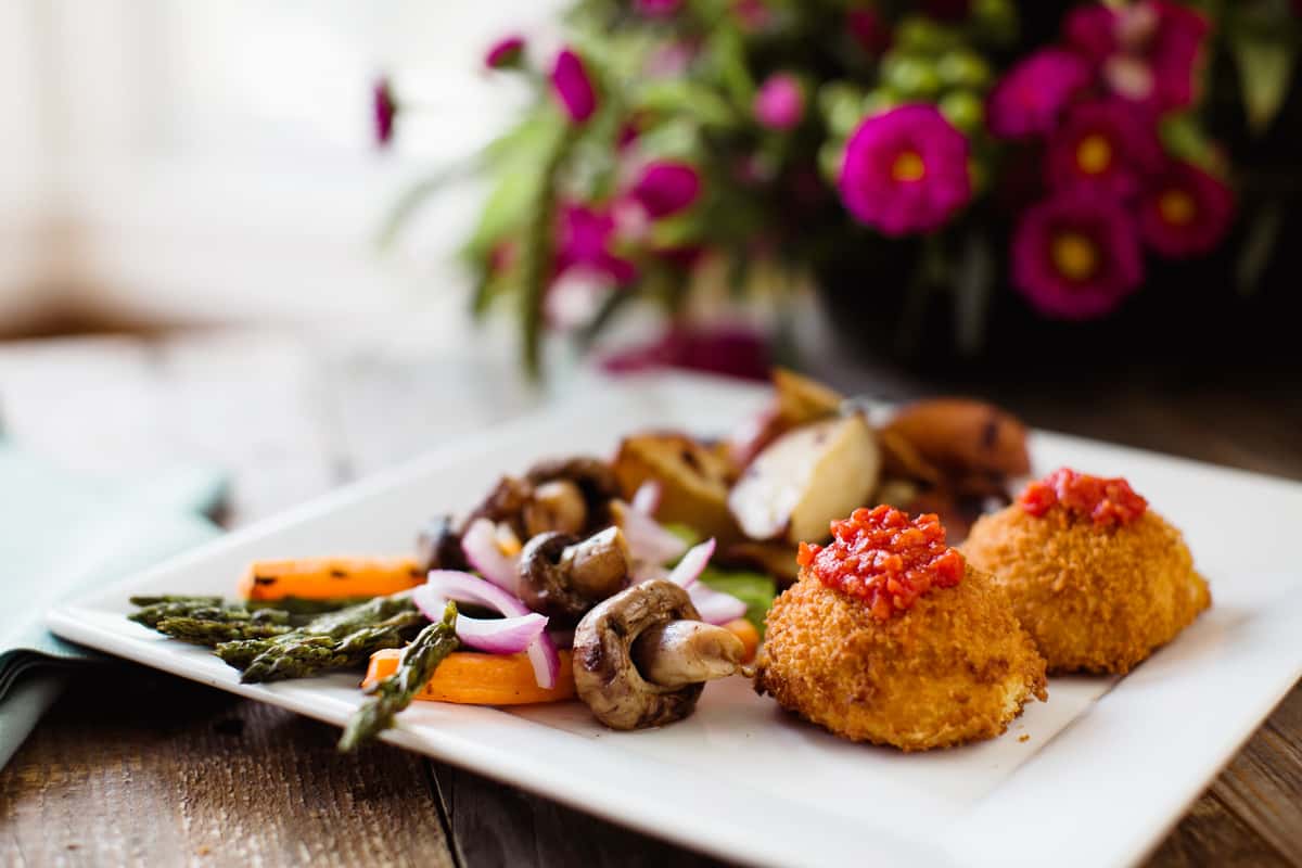 A beautifully plated dish for wedding catering events, featuring crispy appetizers, sautéed vegetables, and vibrant garnishes, set against a backdrop of colorful flowers.