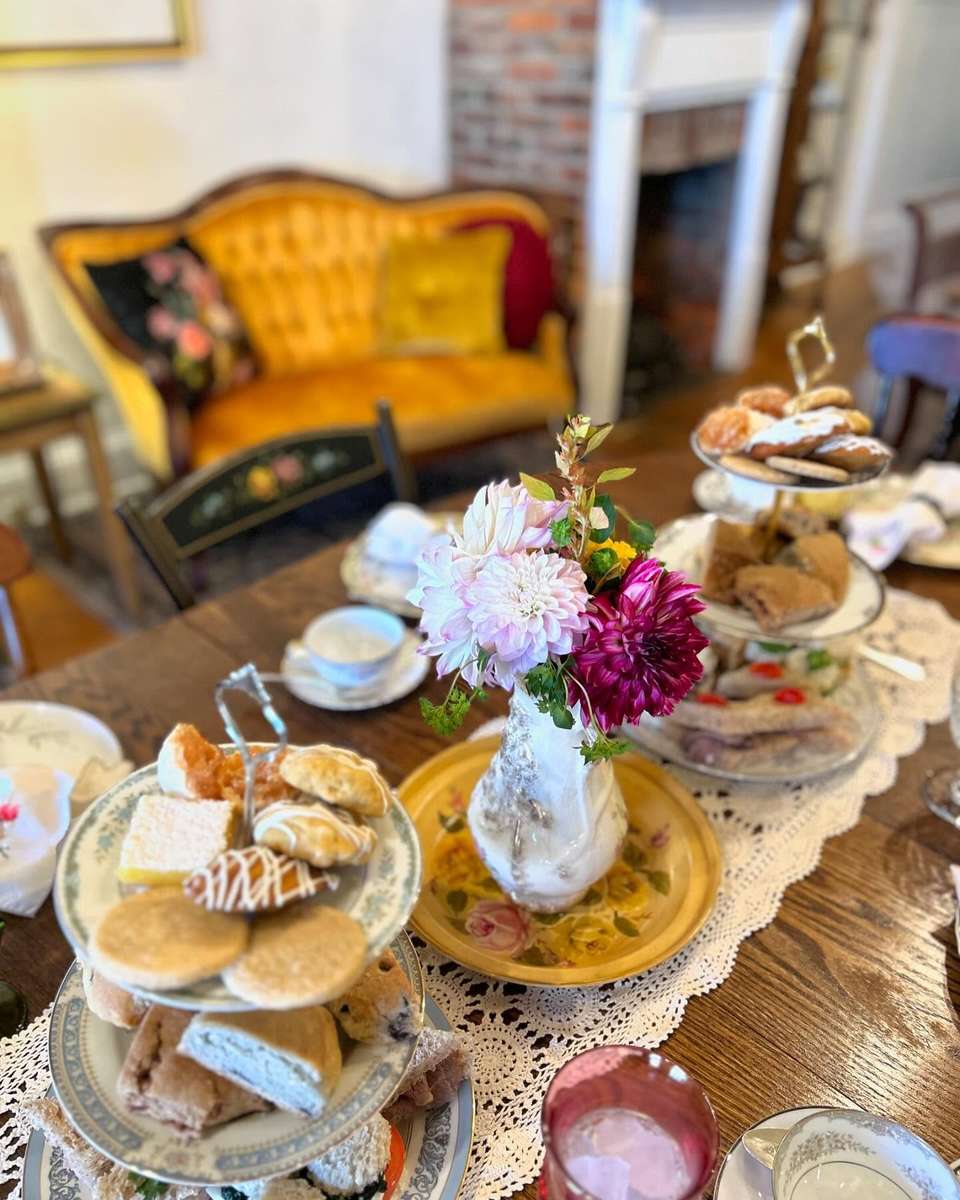 An elegant tea party event setup featuring tiered trays of assorted pastries and cookies, complemented by fresh flowers in a vase, set on a lace tablecloth with vintage teacups.