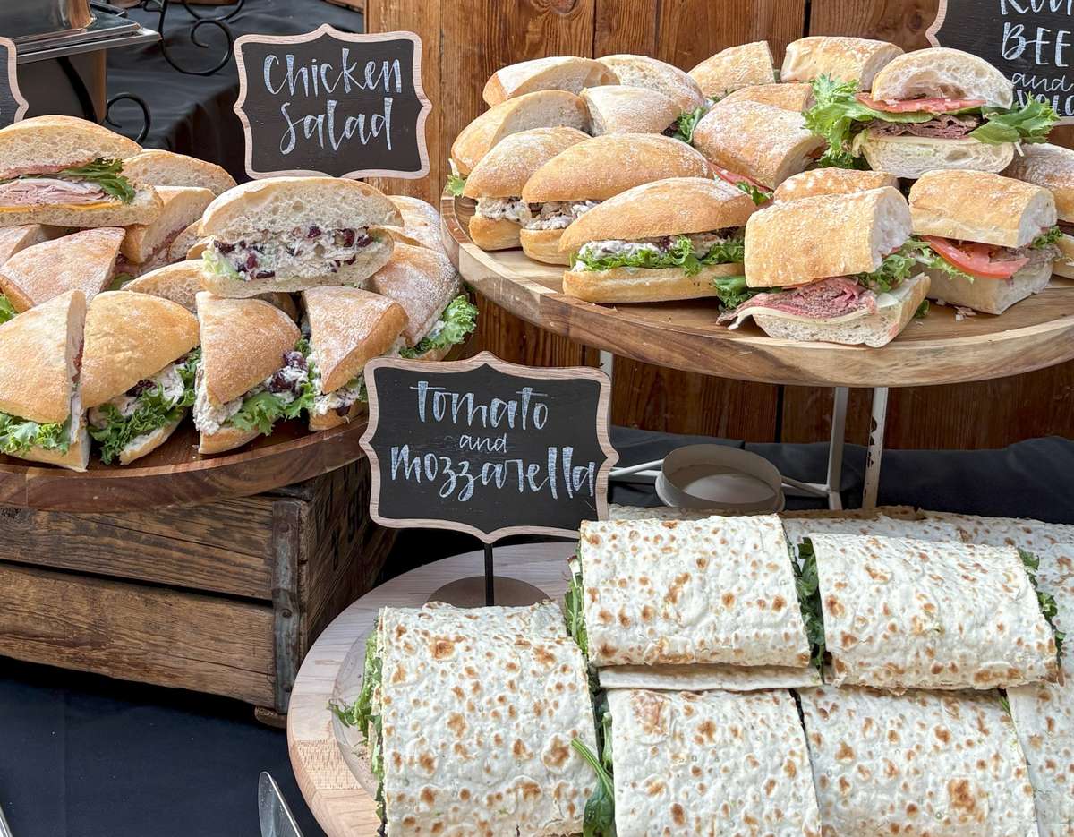 A display of gourmet sandwiches, including chicken salad and tomato mozzarella, arranged on wooden platters, perfect for catering events and gatherings.