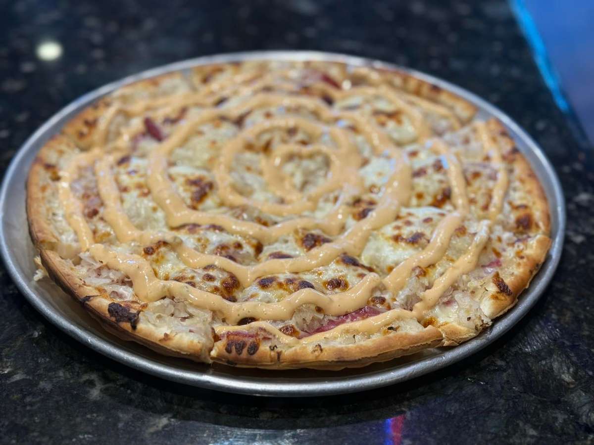 Old Shawnee Pizza's close-up shows a pizza slice with a creamy sauce.