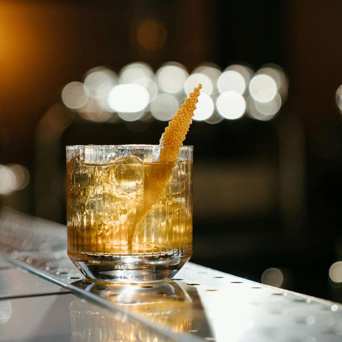 Old Shawnee Pizza's cocktail in a rocks glass garnished with a sugared orange peel sits on a bar.