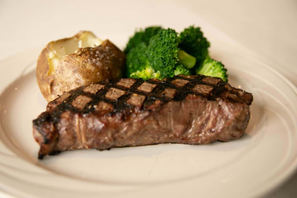 A perfectly grilled steak with beautiful crosshatch grill marks, cooked to a juicy finish and served with a side of vibrant green broccoli. The dish is presented simply, highlighting the rich, savory flavor of the meat and the freshness of the vegetables for a classic and satisfying meal.