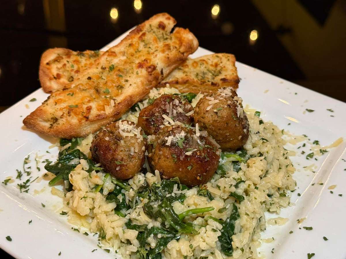 Parmesan-topped meatballs over creamy spinach risotto, served with cheesy garlic bread on a square white plate.