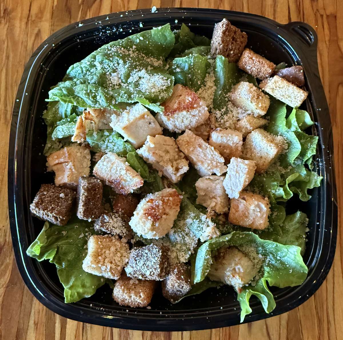 A Caesar salad with chicken and croutons served in a black container from Main Street Eats.