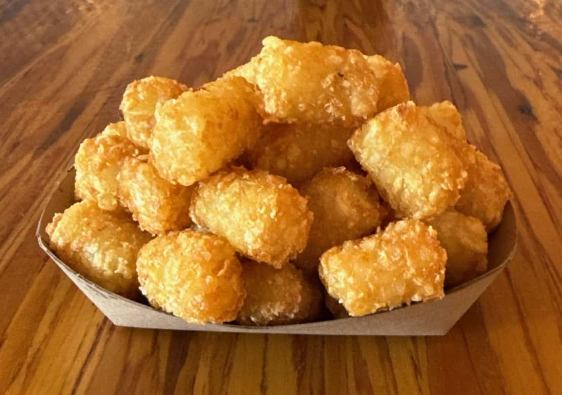 A pile of crispy, golden tater tots served in a cardboard tray at Main Street Eats.