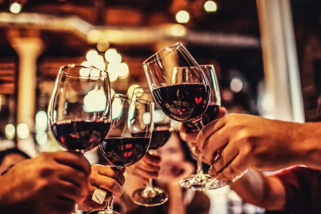 A group of hands cheering wine glasses filled with red wine