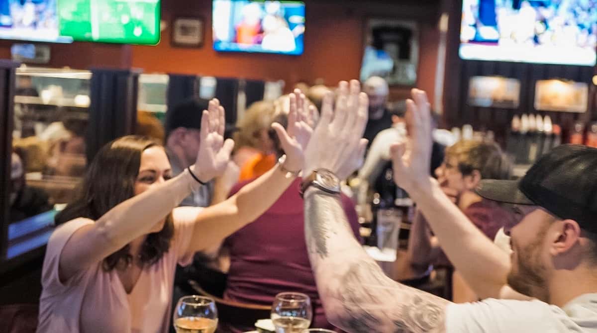 Friends raising their hands and high-fiving over drinks at a restaurant table