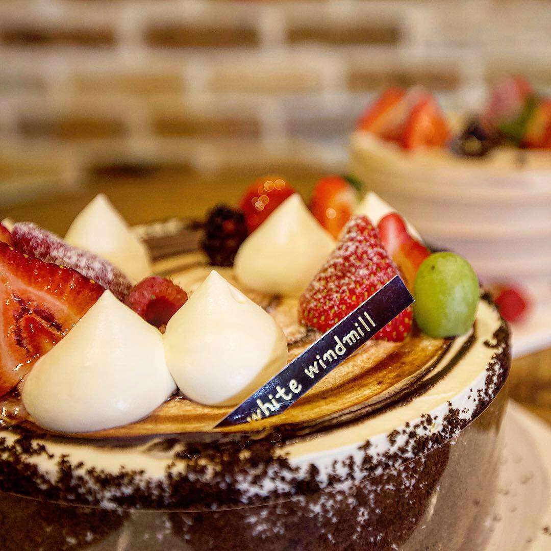 White Windmill chocolate cake topped with whipped cream, fresh strawberries, mixed berries, and green grape