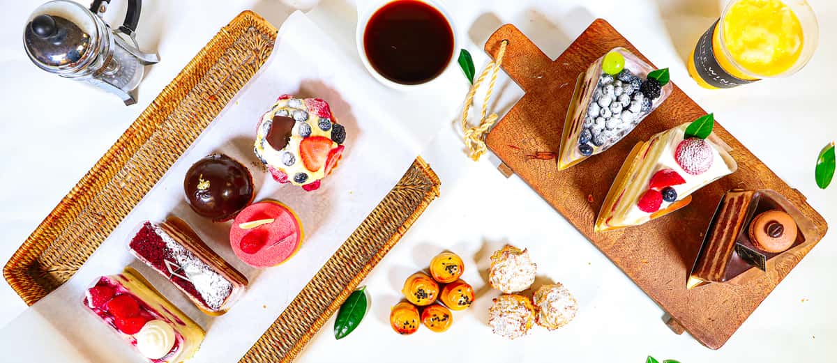 Overhead display of assorted cakes and pastries with coffee, berry slices, chocolate mousse, and small buns on trays