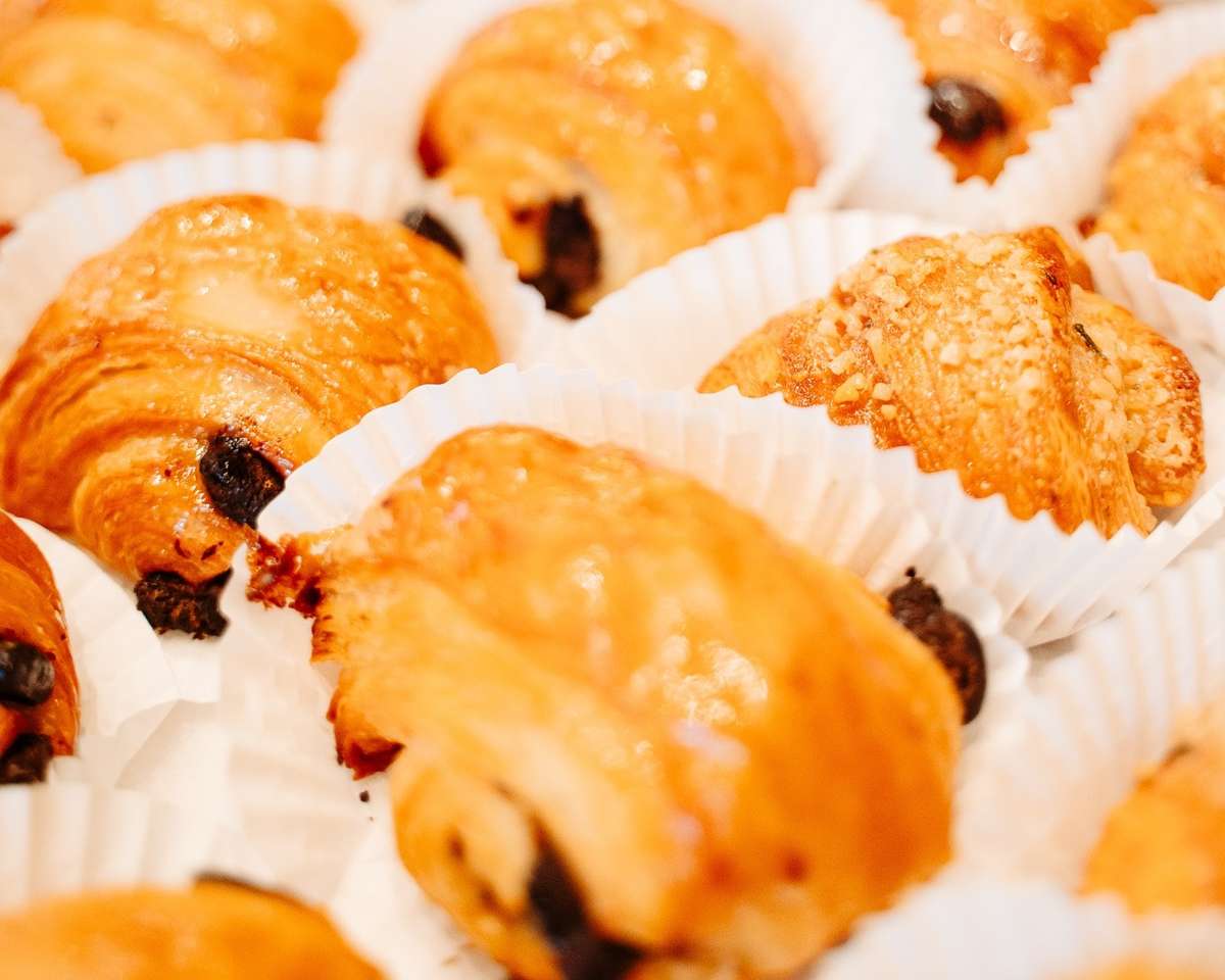 Assorted mini chocolate croissants in white paper cups, golden and flaky with visible chocolate filling