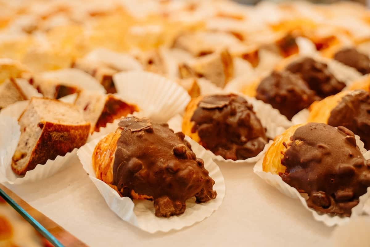Chocolate-covered croissant bites in paper cups on bakery display, topped with crunchy chocolate pieces