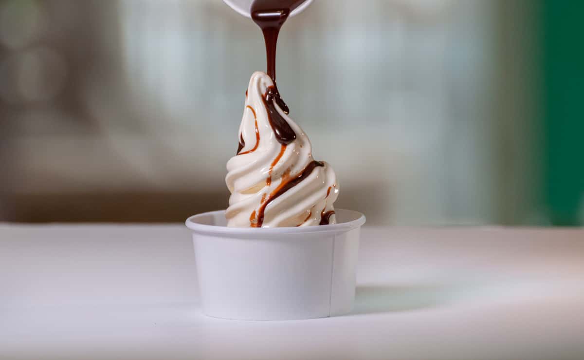 A close-up of ice cream with chocolate topping dripped over the top on a table