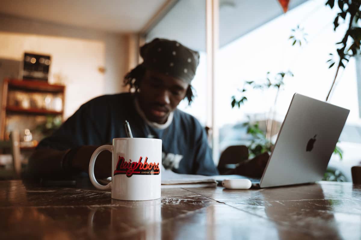 A person works on a laptop with a coffee cup nearby at Neighbors Coffee. The cup reads "Neighbors COFFEE COMPANY" in cursive.