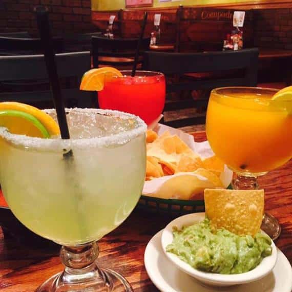 margarita with a straw, two other drinks with chips and guacamole
