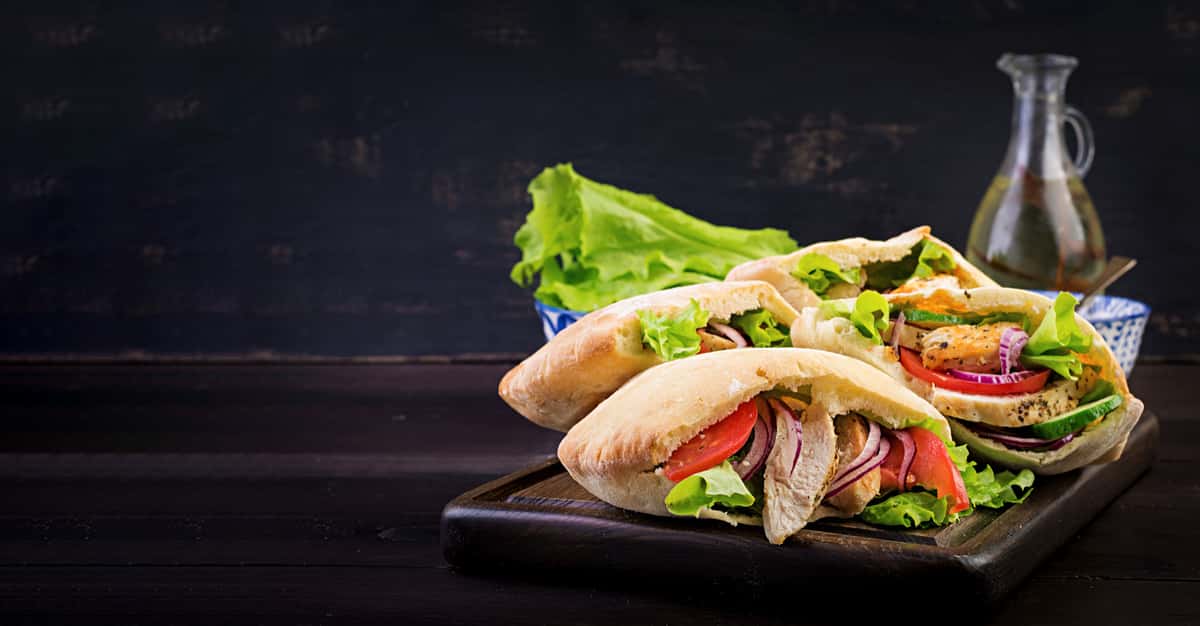 Pita stuffed with chicken, tomato and lettuce on wooden table. Middle Eastern cuisine.