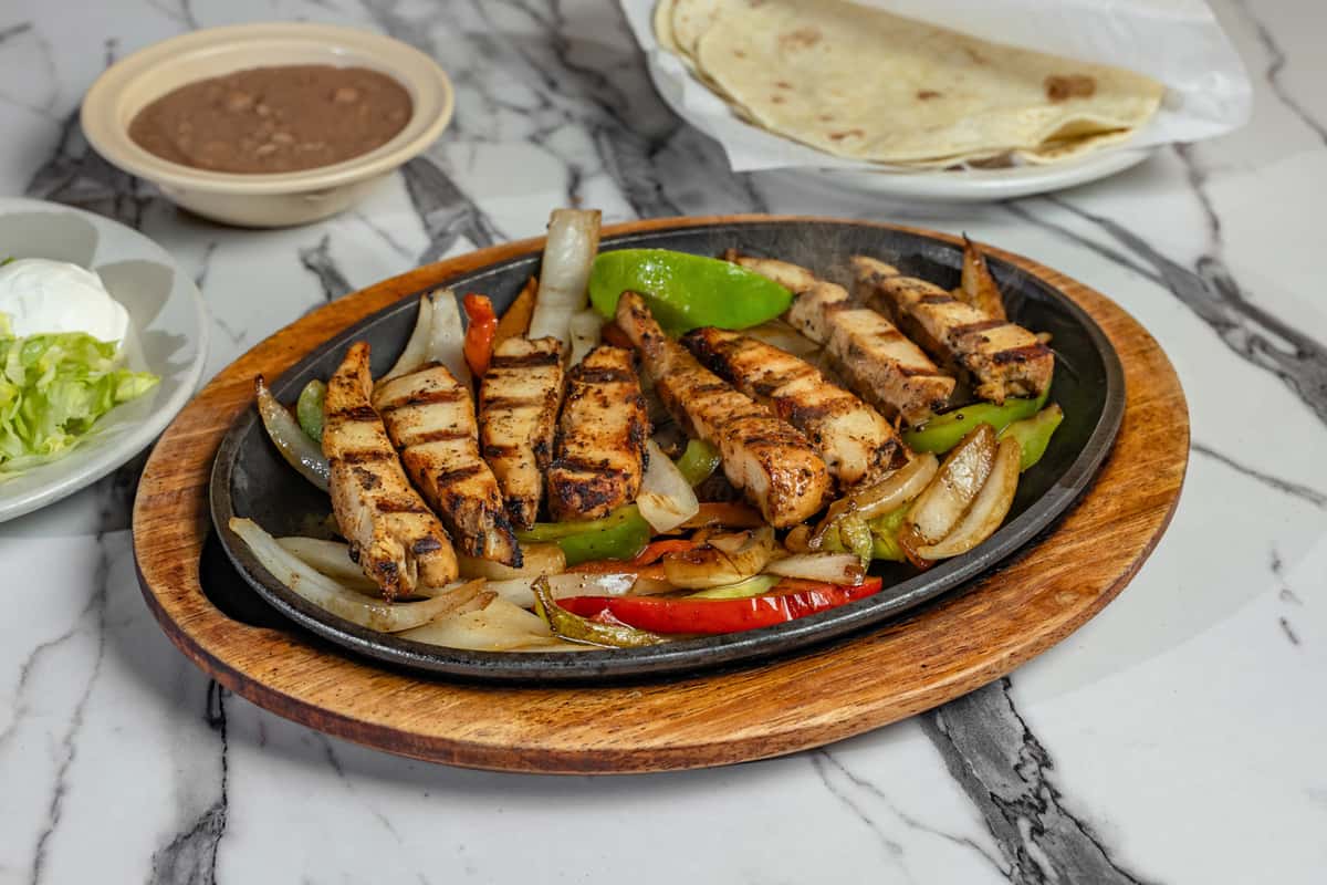Sizzling grilled chicken fajitas served on a hot skillet with sautéed bell peppers and onions, paired with refried beans, shredded lettuce, sour cream, and warm flour tortillas — classic Tex-Mex dish perfect for customizable wraps.