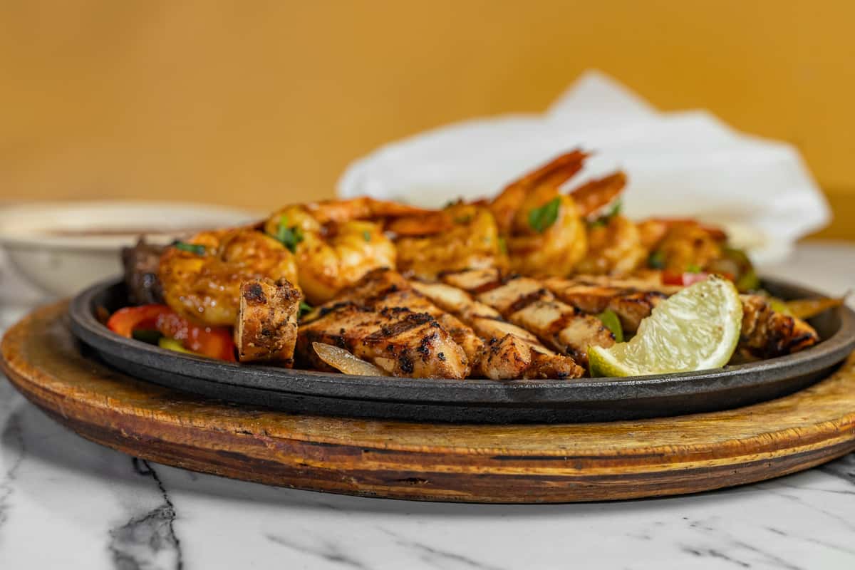 Grilled chicken and shrimp fajitas on a steaming hot skillet with lime wedge, served over sautéed bell peppers and onions.