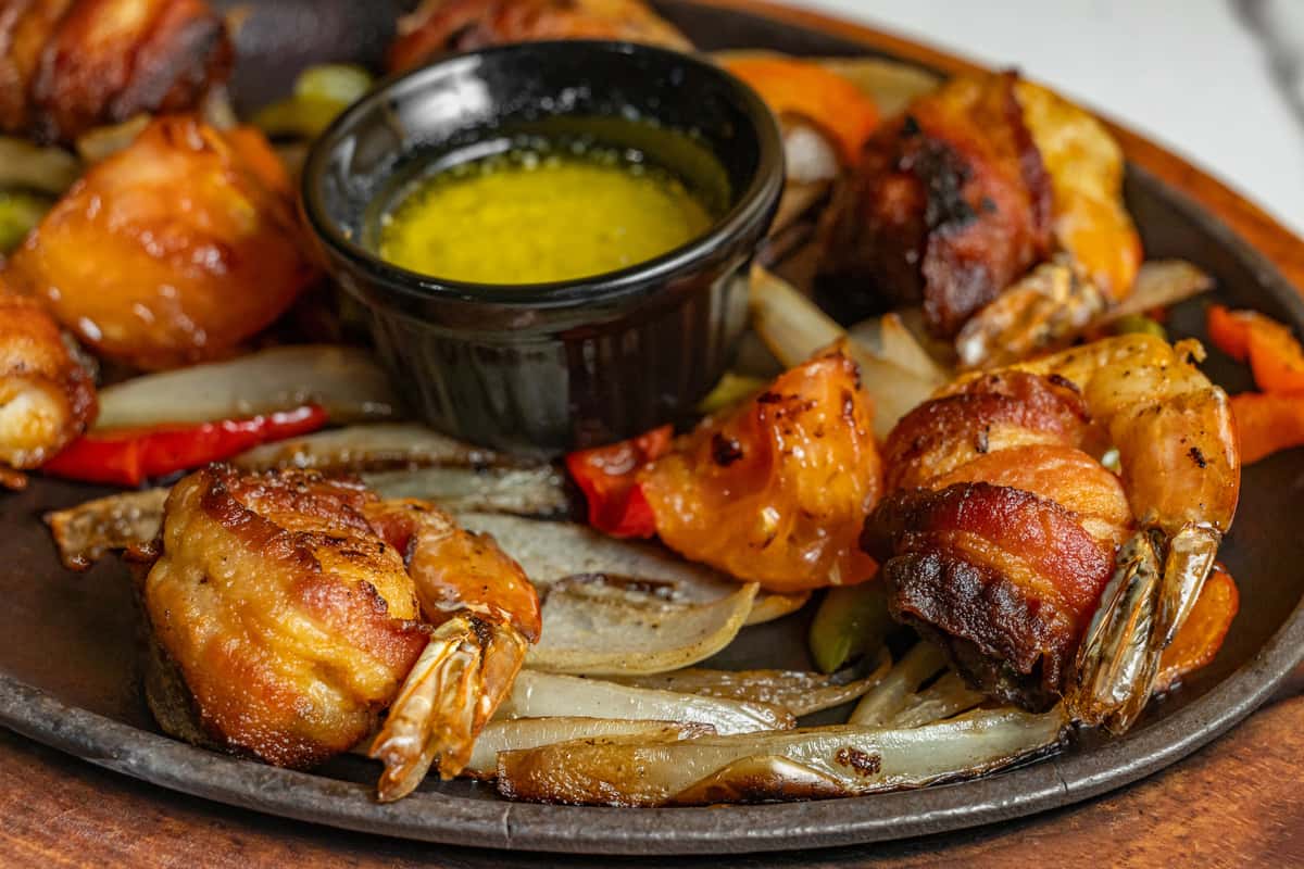 Sizzling bacon-wrapped shrimp fajitas served on a hot skillet with grilled onions, bell peppers, and a side of golden garlic butter — a bold Tex-Mex appetizer bursting with smoky flavor.
