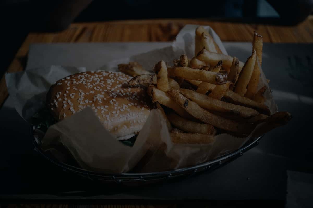 A tempting burger with sesame seed bun and crispy fries served in a basket on a wooden table.