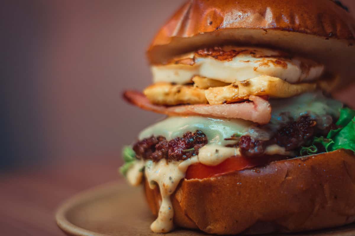 Gourmet bacon cheeseburger with a beef patty, fried egg, lettuce, tomato, and creamy sauce on a brioche bun.