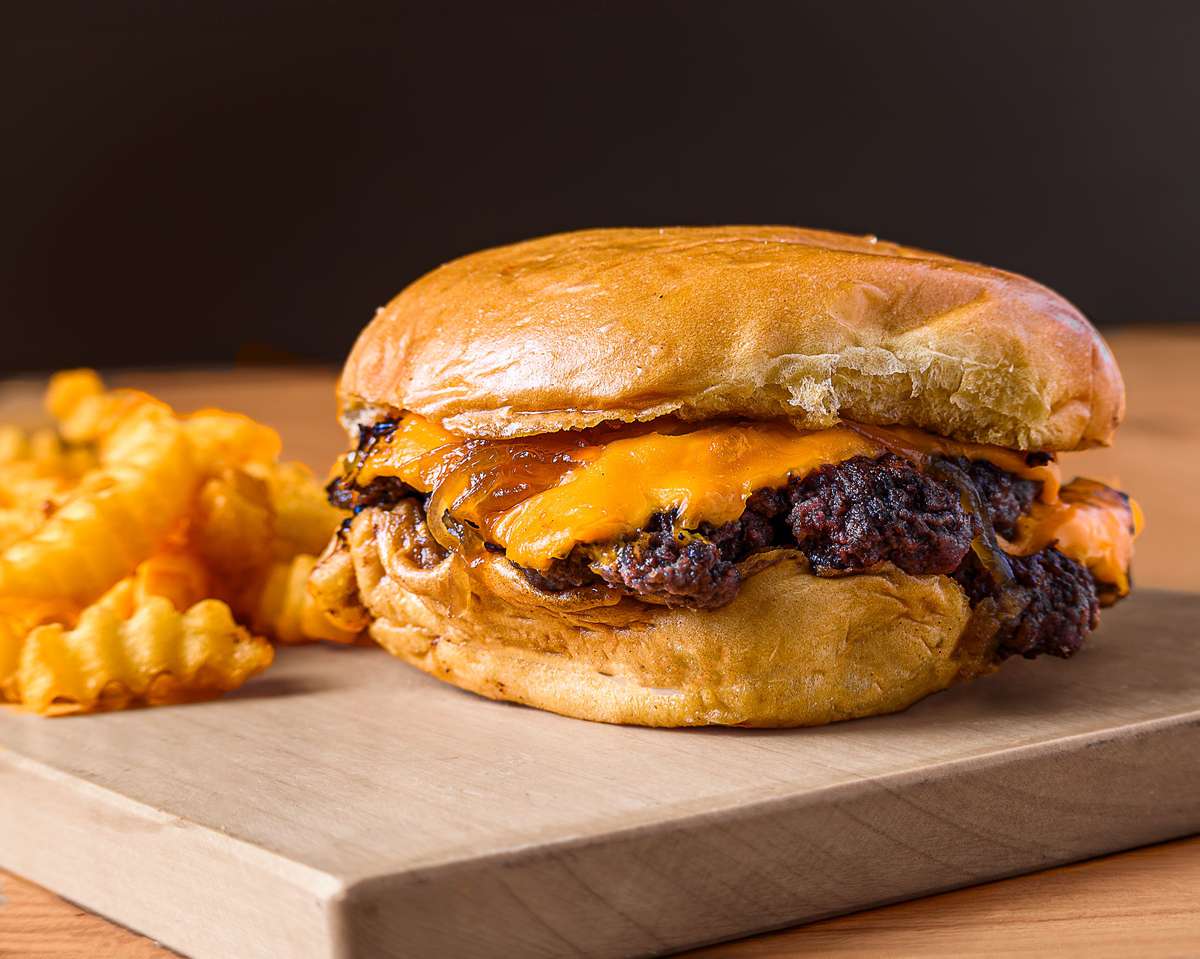 Tasty cheeseburger with crinkle-cut fries presented on a wooden board, perfect for fast food lovers.