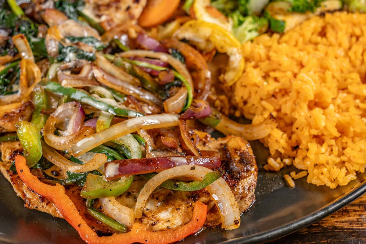 Grilled chicken breast smothered with sautéed bell peppers and onions, served with seasoned Mexican rice and a medley of steamed vegetables—perfect for a hearty and flavorful Tex-Mex entrée.