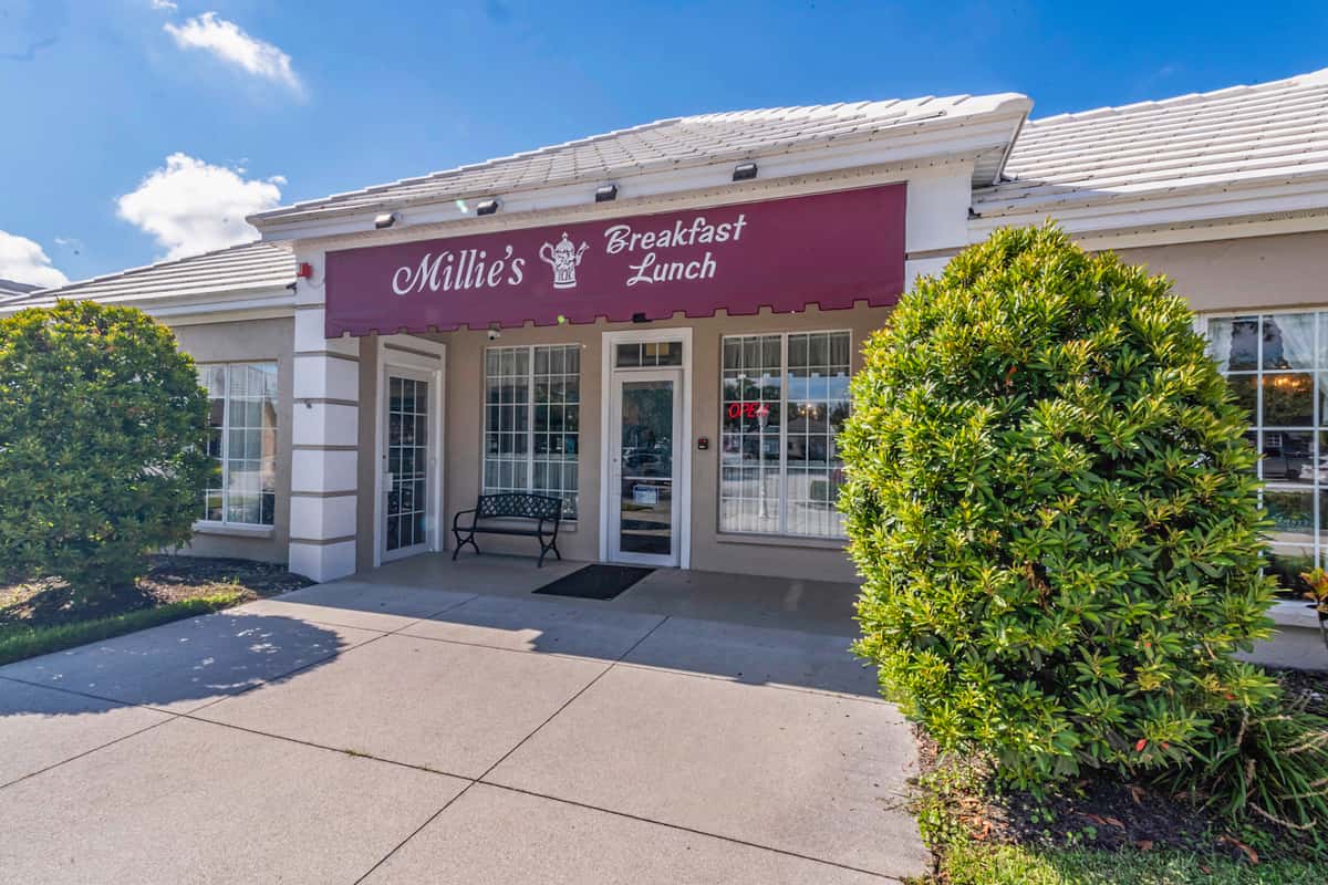 Exterior of Millie's Breakfast & Lunch restaurant with a maroon awning, white trim, and a welcoming entrance framed by large green shrubs — a cozy daytime dining spot ideal for casual breakfast or brunch gatherings.