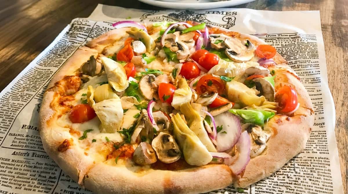 Vegetable pizza with white cheese, artichoke hearts, mushrooms, cherry tomatoes, and red onions.