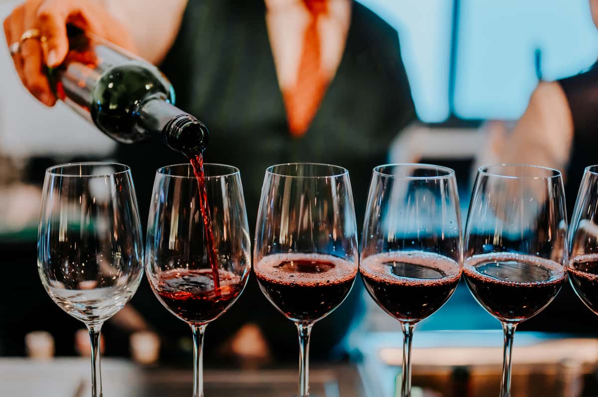 Bartender pouring red wine into a row of wine glasses